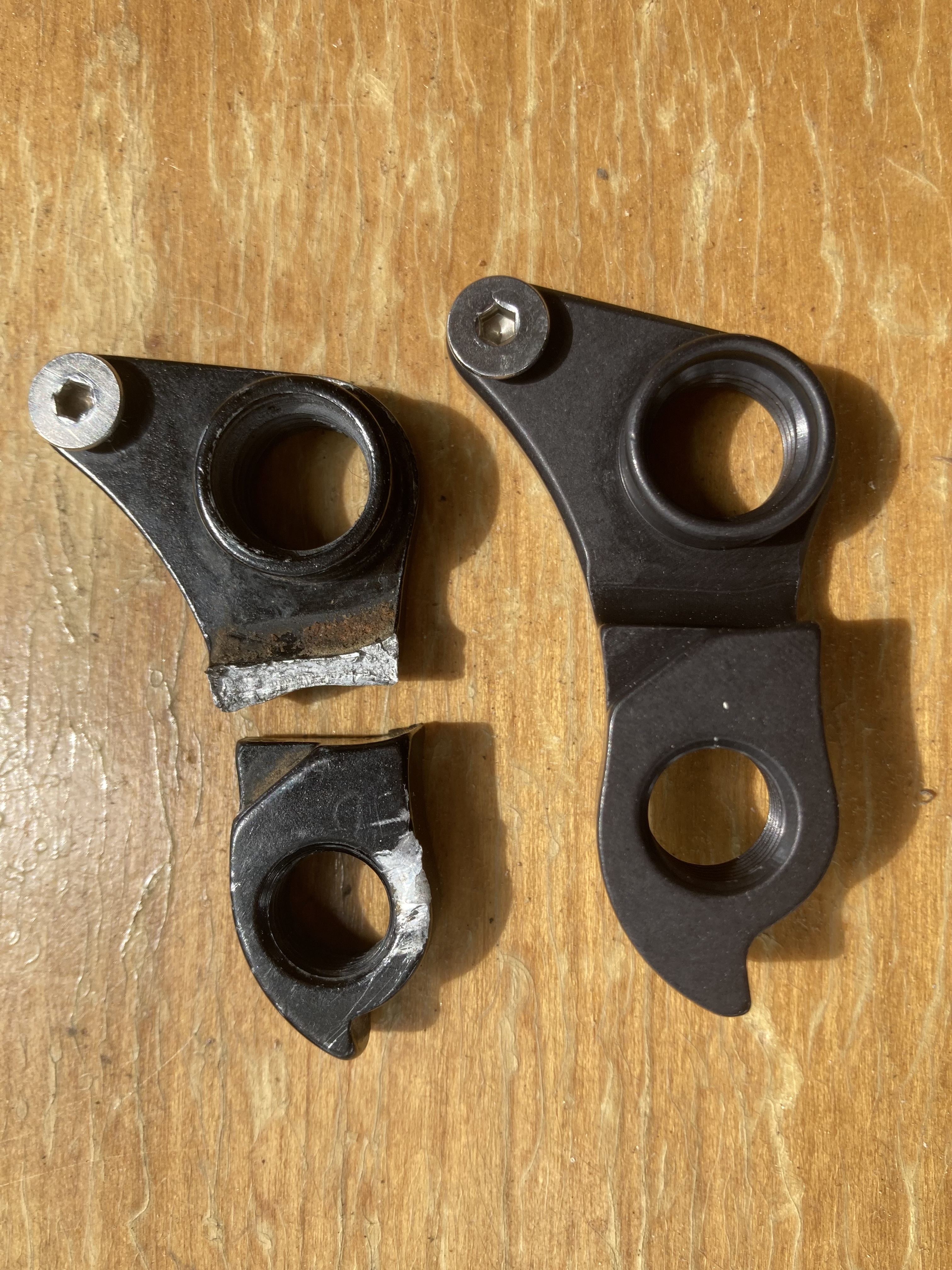 Broken derailleur hanger on the left beside an intact replacement on the right
