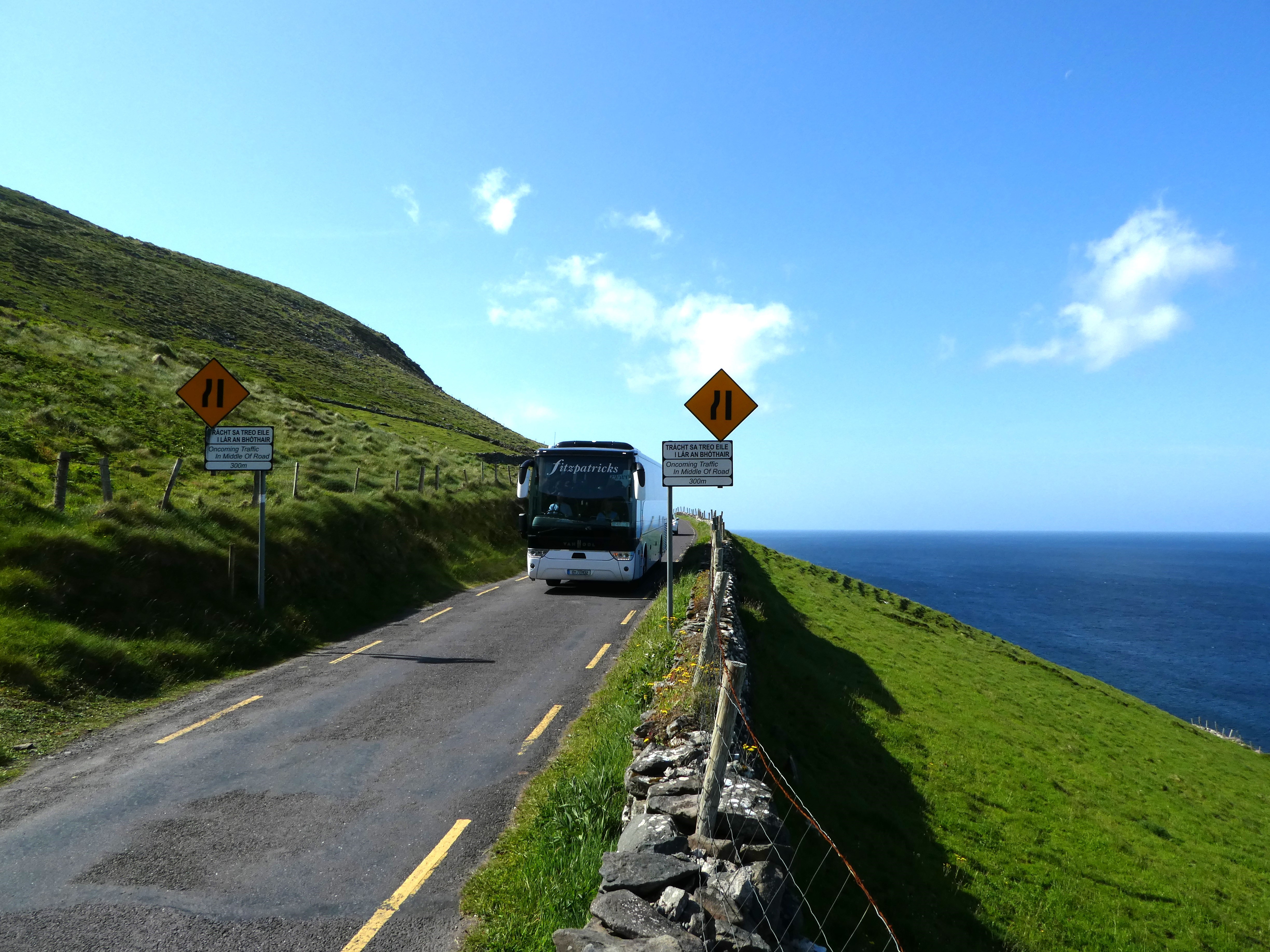 A narrow coastal road at Slea Head with a coach and warning signs in May 2024